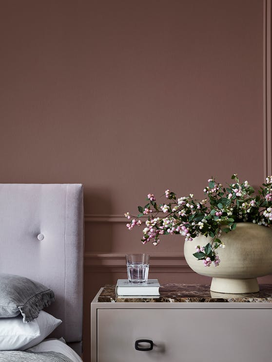 Bedroom painted in warm neutral red (Nether Red) with contrasting grey woodwork and a bed scattered with cushions.