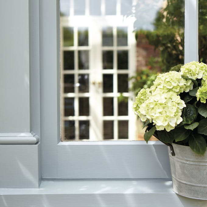 Light blue exterior window frame with a flower pot on the window sill and a white panelled door visible in the reflection.