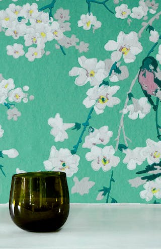 Close-up of green floral wallpaper (Massingberd Blossom - Verditer) featuring birds with white vases in the foreground.