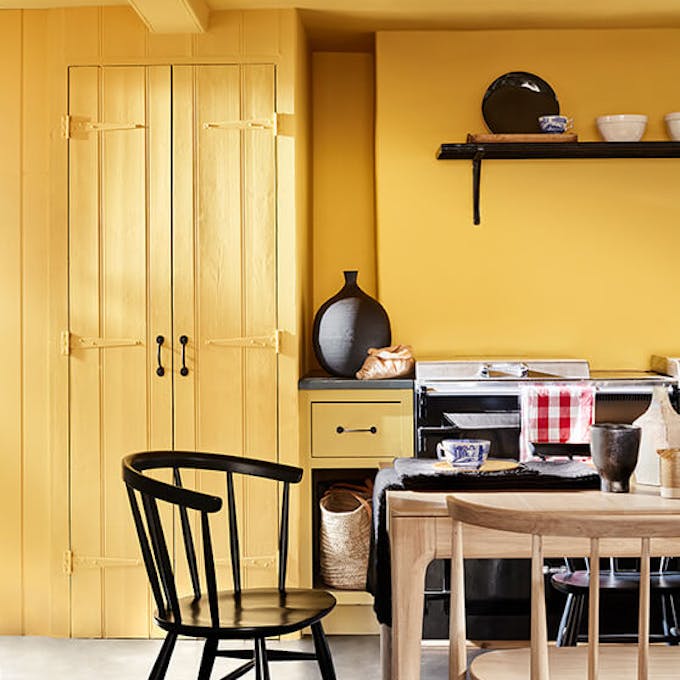 Kitchen color drenched in vibrant yellow shade 'Giallo', with a wooden table and chairs.