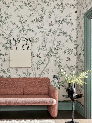 Living room with an off-white bird print mural wallpaper (Belton Scenic - Oyster) with a pink sofa and small table.