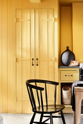 Kitchen color drenched in vibrant yellow shade 'Giallo', with a wooden table and chairs.