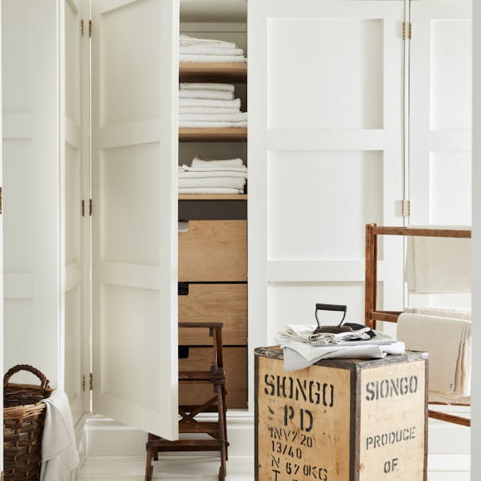 Laundry room color drenched in off white 'Linen Wash' with the closet door opened showing wooden drawers and folded laundry.