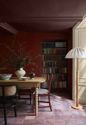 Dining room painted in cherry red shade 'Bronze Red' with a crimson ceiling (Arras) above wooden dining furniture and a book shelf.