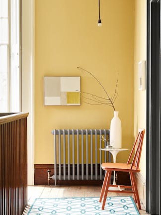 Hallway decorated with Light Gold walls, grey radiator, an orange chair, a patterned rug, and a white side table and vase.