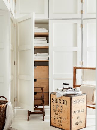 Laundry room color drenched in off white 'Linen Wash' with the closet door opened showing wooden drawers and folded laundry.