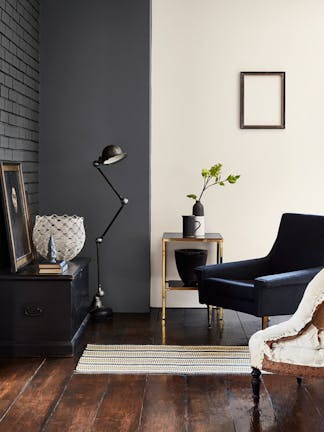 Living room with a two-tone wall in dark grey and off-white and a black leather chair opposite grey-black striped wallpaper.