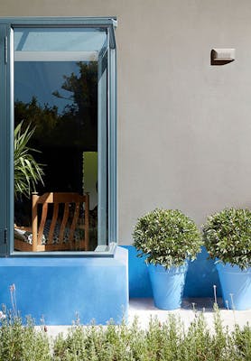 House exterior with a large window, walls painted in neutral grey (Slit) and bright blue (Tivoli), and matching plant pots.