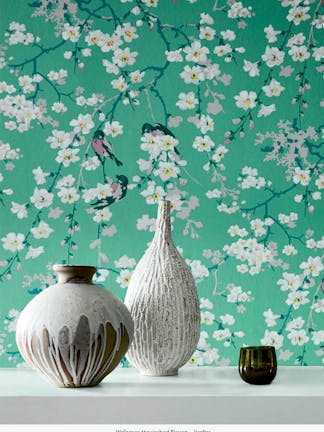 Close-up of green printed floral and bird wallpaper (Massingberd Blossom - Verditer), with two ornaments in front.