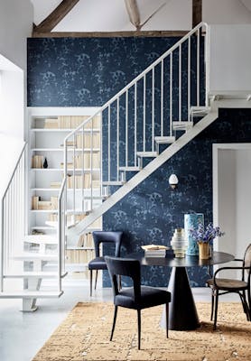 Hallway with dark blue damask wallpaper (Tulip - Blue Black), a black table and chairs, and white stairs passing a bookcase.