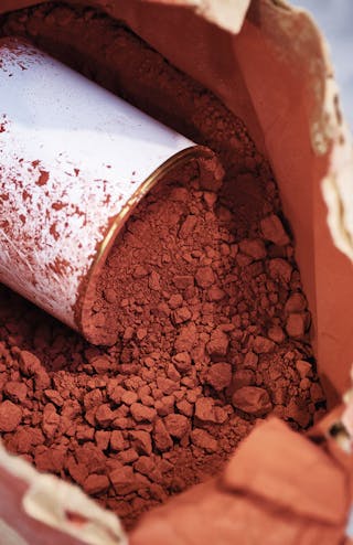 A brown paper bag containing brown powder, with a white paint tin resting inside.