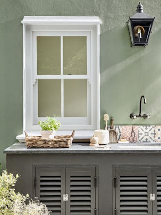 Outside kitchen sin area in grey green 'Boringdon Green' with a contrasting grey cabinet and white window frame.