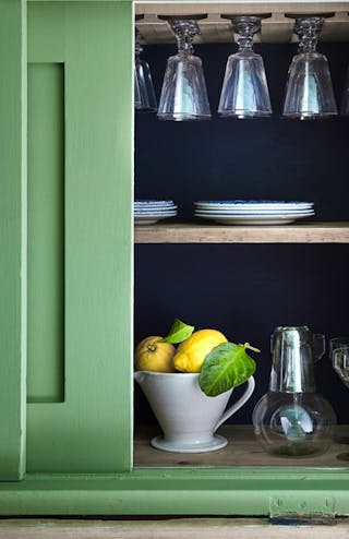 Close-up of deep green kitchen cupboards painted in 'Garden', and partly open revealing two lemons and glassware inside.