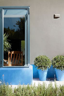 House exterior with a large window, walls painted in neutral grey (Slit) and bright blue (Tivoli), and matching plant pots.