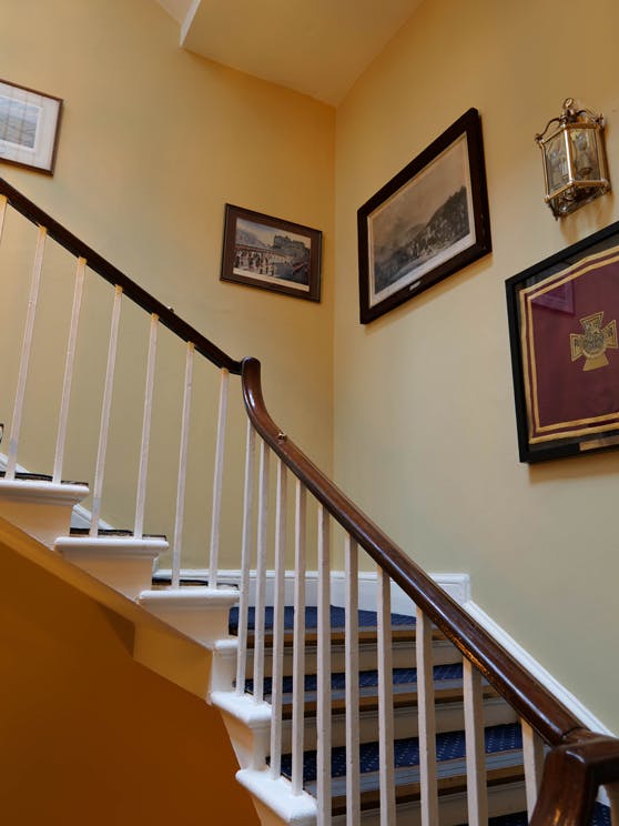 Staircase inside the Horse Guards building featuring warm yellow Sunlight painted walls with historic paintings.