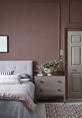 Bedroom painted in warm red (Nether Red) with contrasting grey woodwork and a bed scattered with cushions.