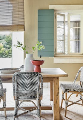 Golden yellow (Bath Stone) dining space with contrasting green shutters, a wooden dining room table and patterned chairs.