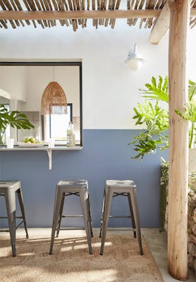 Outdoor breakfast bar with three stools against a wall painted in deep blue (Juniper Ash) and neutral white (Slaked Lime).