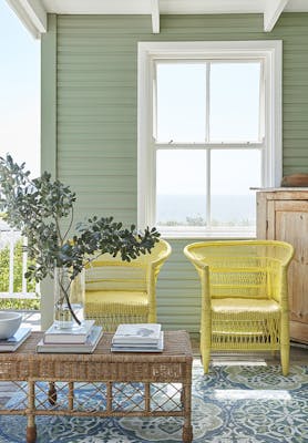 Outdoor living space with bright yellow (Indian Yellow) wicker chairs in front of an 'Aquamarine - Deep' painted cladded wall with a large window.