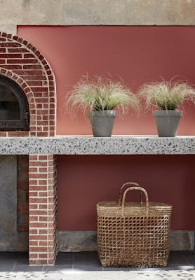 Outdoor kitchen painted in deep terracotta red 'Tuscan Red' with brickwork, plants and a basket.