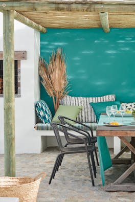 Outdoor table and chairs under a bamboo roof with the back wall painted in blue-green shade 'Canton'.