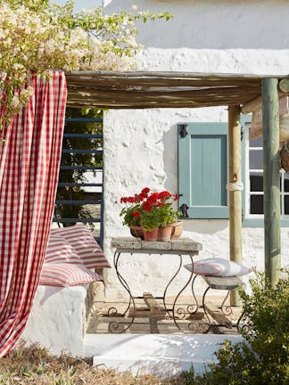 Yard with exerior wall in off white Wood Ash and pale blue shutters (Celestial Blue) with a seating area surrounded by trees.