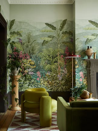 Living space featuring green tropical mural wallpaper (Capricorn - Boringdon) with a green armchair and sofa next to a fireplace.