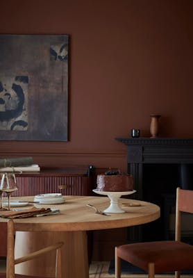 Dining space colour drenched in deep brown shade 'Ganache' with a wooden table and chairs under abstract wall art.