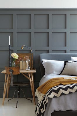 Paneled bedroom painted in dark grey 'Scree' with a small wooden desk next to a grey bed on a white floor.