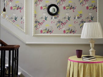 Bottom of stairs with grey bird print wallpaper (Voliéres - French Grey) and a small table with yellow gingham tablecloth.