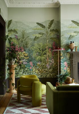 Living space featuring green tropical mural wallpaper (Capricorn - Boringdon) with a green armchair and sofa next to a fireplace.