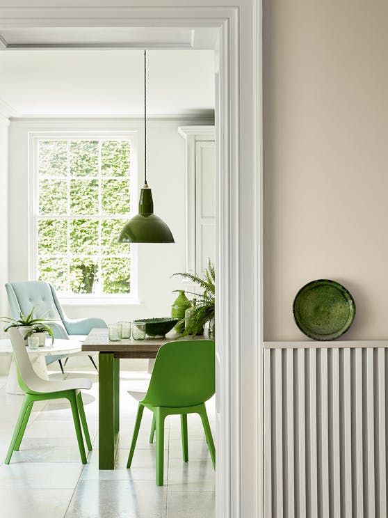 Hallway looking into a dining room painted in beige shade Portland Stone - Dark with bright green dining room chairs.