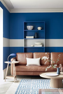 Living space with rich blue (Mazarine) wall and a contrasing neutral (Cool Arbour) stripe  with a tan leather sofa.