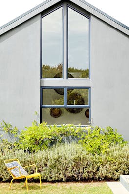 House exterior with large windows painted in mid grey (Urbane Grey) with bright yellow garden chair and plants.