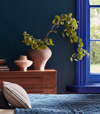 Bedroom painted in rich blue shade 'Royal Navy' with a bright blue 'Smalt' window frame, dark blue on the ceiling and a bed under the window.