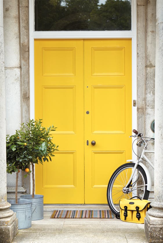 Front door painted in bright yellow 'Mister David' with two trees and a bike under pillars.