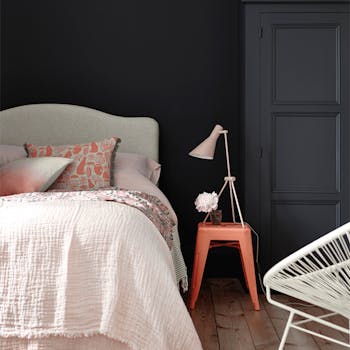 Bedroom painted in blue black 'Basalt' with a light pink bed and a contrasting bright orange stool.