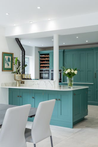 A kitchen with green kitchen cupboards in Pleat, marble worktops and walls painted in a bright white.