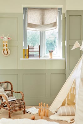 Children's nursery painted in 3 different shades of green neutral 'Green Stone' with childrens toys and a small wicker chair.