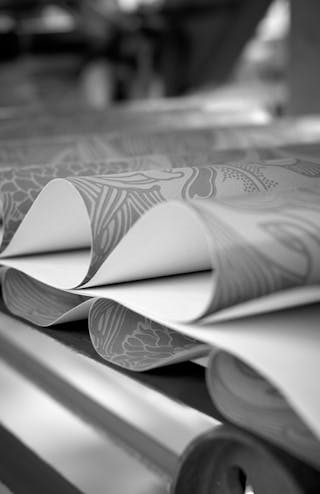 A black and white short of sheets of wallpaper rolled on top of each other on an assembly line.