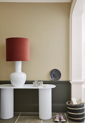 Pale brown neutral hallway (Lute) with lower wall painted in grey green (Pompeian Ash) and a white side table and large lamp.