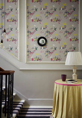 Bottom of stairs with grey bird print wallpaper (Voliéres - French Grey) and a small table with yellow gingham tablecloth.