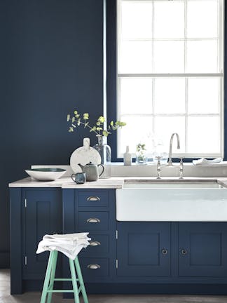 Kitchen painted in dark blue (Hicks' Blue) with a contrasting bright green (Green Verditer) stool underneath a window.