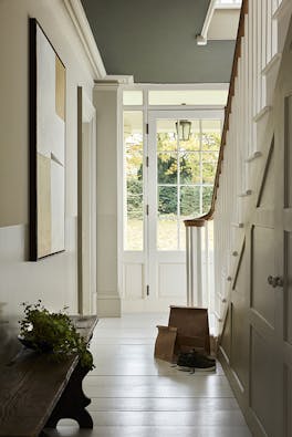 Hallway painted in four graduating shades of neutral 'Portland Stone' with a white wooden floor and a staircase to the right, looking out to a garden.