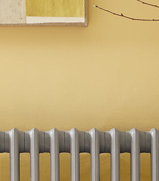 Close-up of Light Gold walls, a grey radiator, an orange chair, a patterned rug, and a white side table and vase.