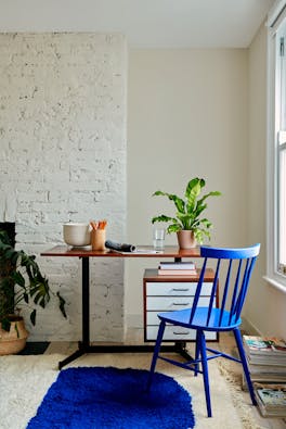 Home office with pale taupe brickwork wall (Joanna), a vibrant blue wooden chair and a matching rug in front of wooden desk.