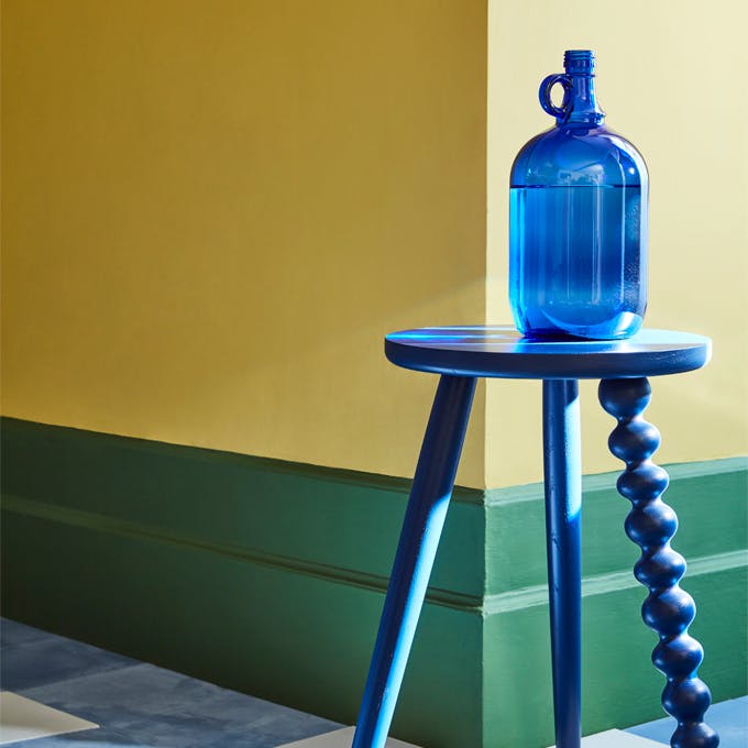 Dining room with vibrant yellow walls (Indian Yellow) with a green baseboard and bright blue stool.