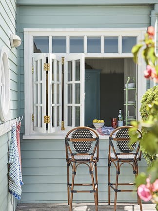 Outside breakfast bar with cladded walls painted in grey blue shade 'Celestial Blue' with two wooden stools under white shutters.