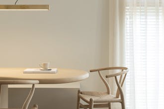 Neutral off-white Portland Stone walls in a dining room with light wooden table and chairs and white translucent curtains.