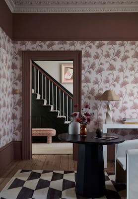 Living space featuring pink floral wallpaper (Mosaic Trail - Blush) with a dark table and chair with a door leading out to a staircase.